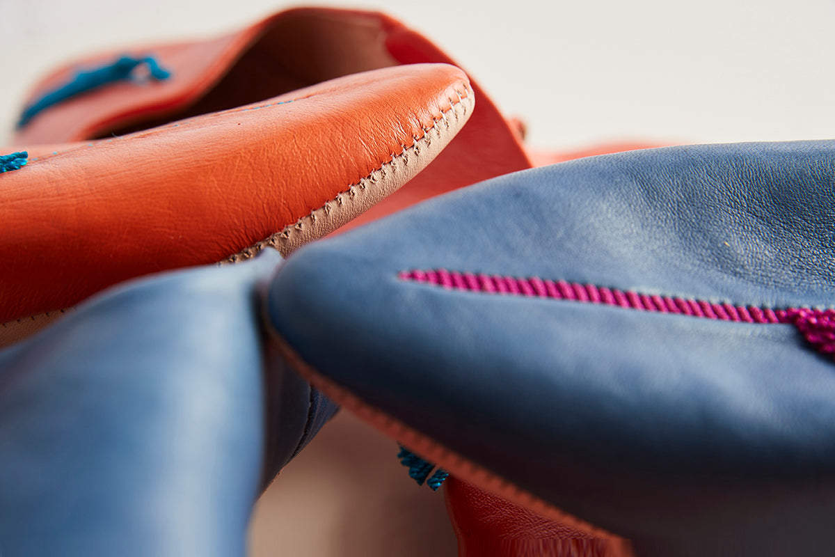Red and blue leather slippers with hand-stitched edges and decorative thread details.