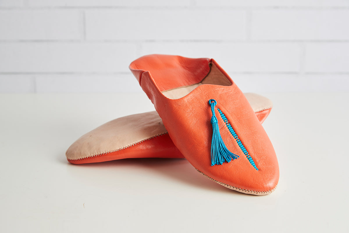 Orange leather slippers with blue tassel decoration and tan interior lining.