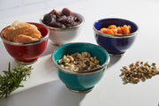 Four glazed bowls in red, gray, blue, and teal with silver trim, each containing different foods and nuts.