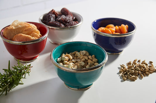Four glazed bowls in red, gray, blue, and teal with silver trim, each containing different foods and nuts.