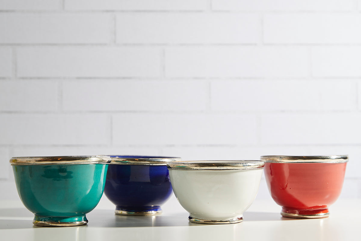 Four glazed bowls in turquoise, navy, cream, and coral with metallic silver trim around the rims.