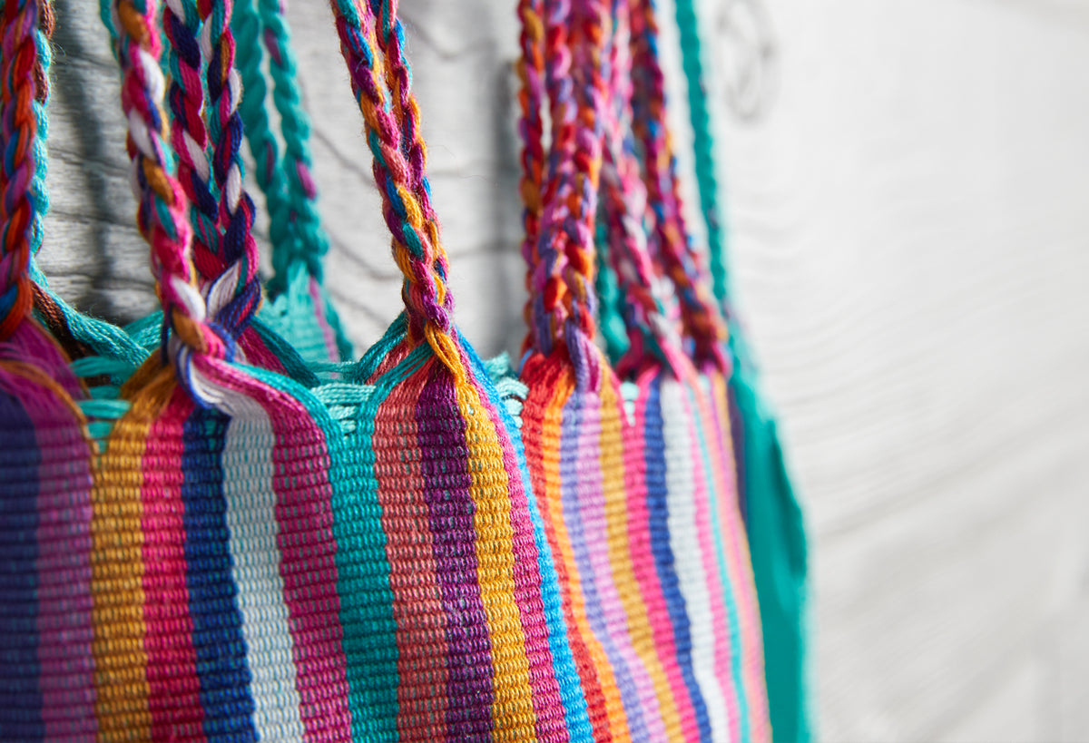 Colorful woven bag with multicolor vertical stripes and twisted cord handles in pink, teal, yellow, and purple.