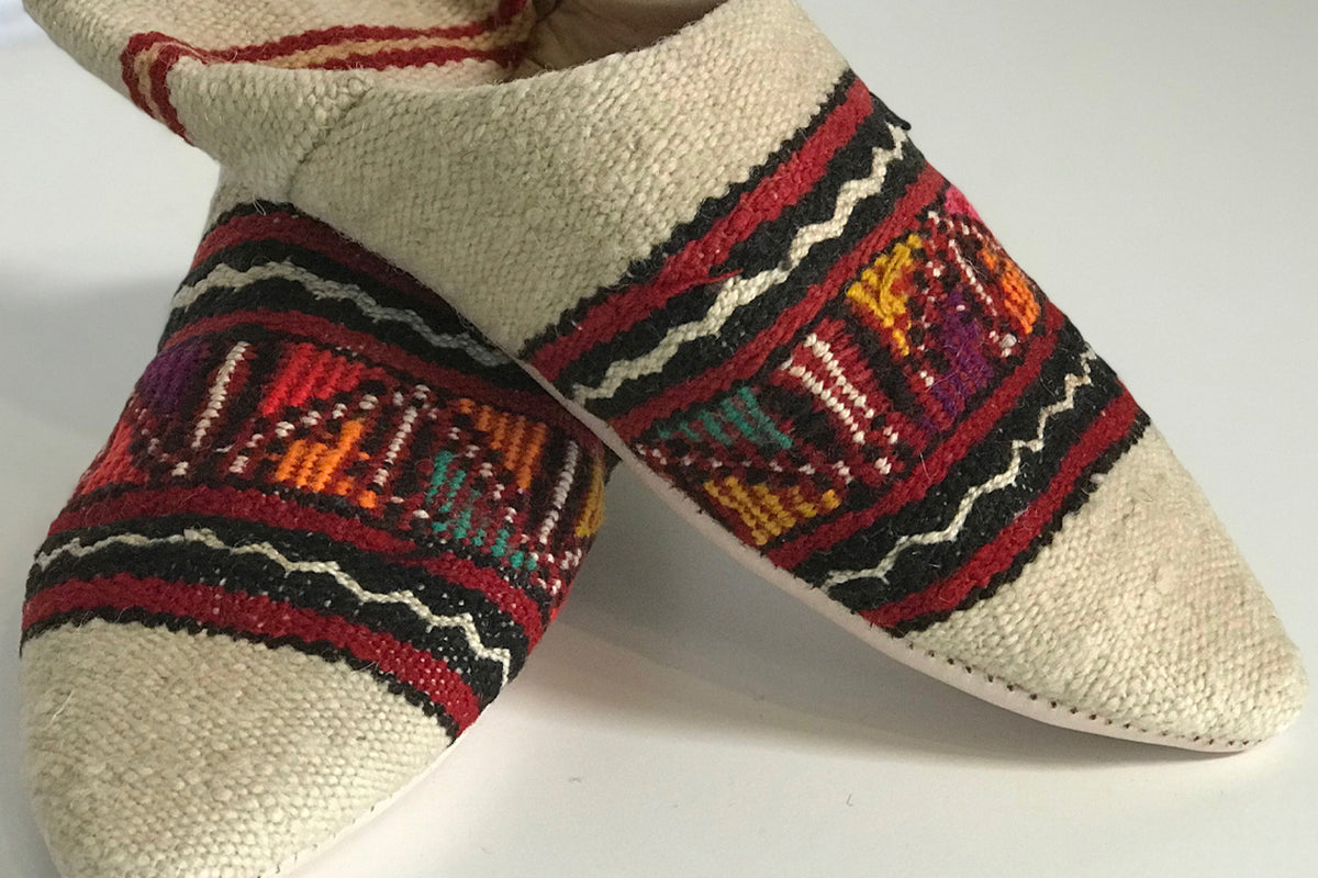 Pair of cream and red kilim slippers with geometric woven patterns in burgundy, orange, and teal.
